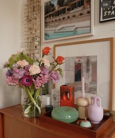 a vase filled with flowers sitting on top of a wooden table next to pictures and candles