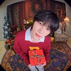 a boy holding a red present box in front of a christmas tree