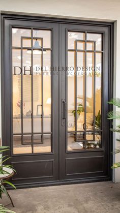 the front door to a building with two glass doors and plants in pots on either side