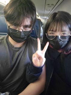 two people wearing face masks and holding up the peace sign in front of their faces