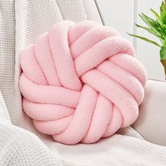 a pink ball of yarn sitting on top of a white couch next to a potted plant