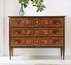 a wooden dresser with two drawers and a vase on it's top, against a white wall