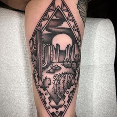 a black and white tattoo on the leg of a person with desert scene in background