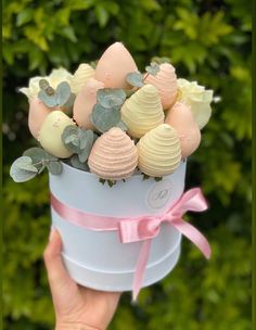 a hand holding a white bucket filled with assorted candies and greenery in it