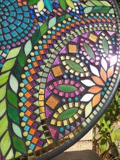 a colorful stained glass plate sitting on top of a wooden table next to a bush