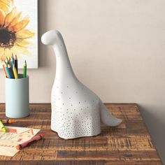 a white dinosaur shaped pencil holder sitting on top of a wooden table next to a cup with colored pencils in it