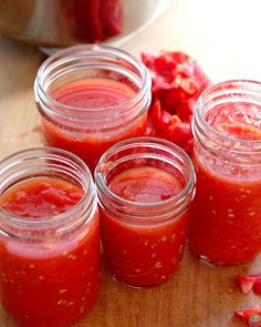 four jars filled with red sauce sitting on top of a wooden table