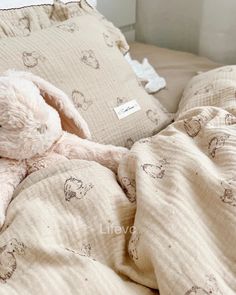 a white stuffed animal laying on top of a bed covered in blankets and pillows,