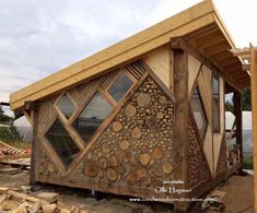 a building made out of wood with windows on the side and logs stacked around it