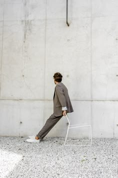 a man in a suit leaning against a wall with his foot on a white chair