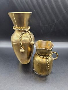 two gold vases sitting next to each other on a gray surface with rope wrapped around them