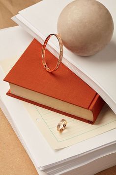 a stack of books with a ring on top of it next to a rock and a ball