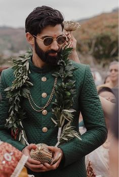 a man in a green suit and gold necklace holding an object while standing next to other people