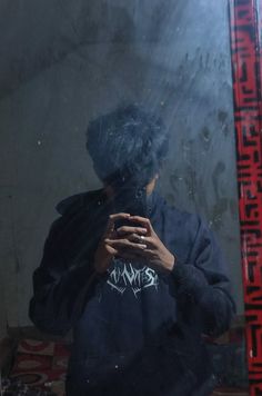 a man standing in front of a mirror looking at his cell phone while wearing a black hoodie