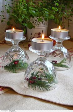 three clear glass candlesticks sitting on top of a white table cloth next to a potted plant