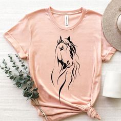 a t - shirt with a horse drawn on it next to a hat and flowers