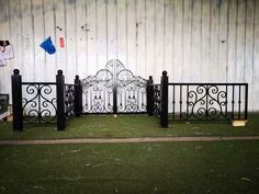 an iron gate is in front of a white fence with black posts on the grass