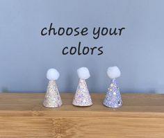 three small party hats sitting on top of a wooden table next to a sign that says choose your colors