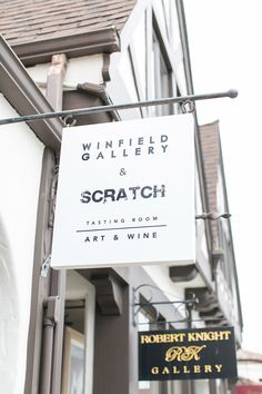 a white sign hanging from the side of a building next to a wine shop and winery