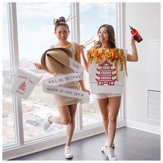 two women dressed in costumes holding signs and posing for the camera, with one holding a drink