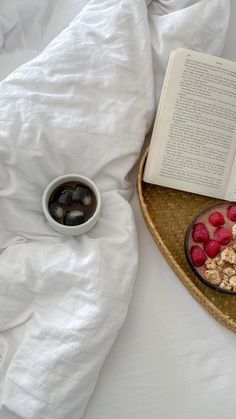 an open book and bowl of berries on a bed