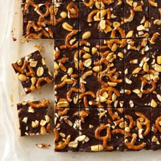 chocolate and pretzel squares are arranged on a sheet of parchment paper, ready to be eaten