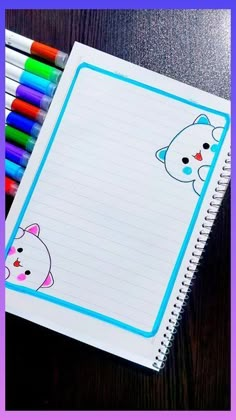 an open notebook with colored pencils on it next to some writing paper and markers