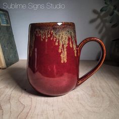 a red and gold coffee mug sitting on top of a table next to a book