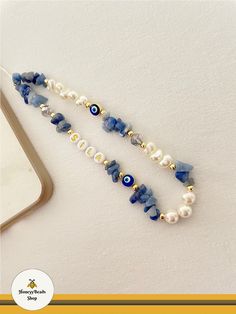 a blue and white beaded necklace with evil eyes on it next to a cell phone