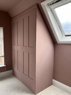 an empty room with pink painted walls and white trim on the window sill, in front of a slanted skylight