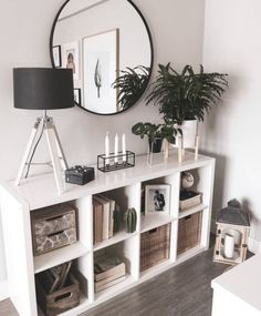 a white bookcase with baskets and plants on it in front of a round mirror