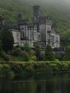 an old castle sitting on top of a lush green hillside next to a body of water