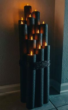 a bunch of lit candles sitting on top of a black stand next to a wall