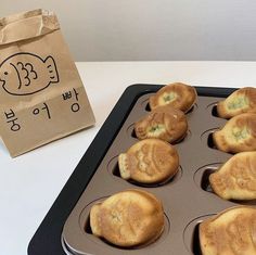 muffins in a pan next to a brown bag on a white counter top