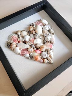 a heart made out of seashells in a black frame on a white table