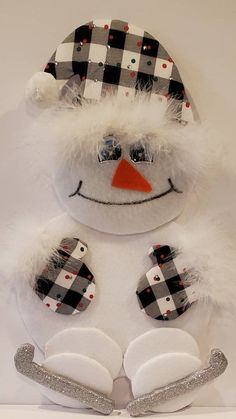 a snowman wearing a plaid hat and mittens on top of a white surface