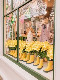 yellow rubber boots are lined up in front of a store window with flowers behind them