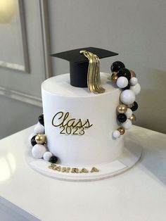 a white graduation cake with black and gold decorations on the top, sitting on a table