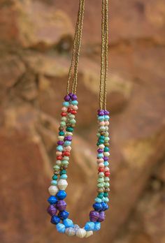 multicolored beaded necklaces hanging from a gold - toned chain on a rock