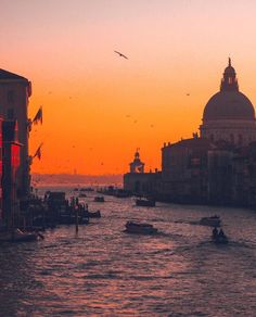 the sun is setting in venice, italy as boats travel down the canal at dusk