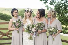 a group of women standing next to each other in front of a wooden fence holding bouquets