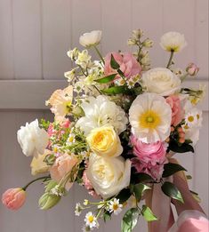 a woman holding a bouquet of flowers in front of a white door with pink and yellow accents