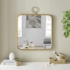 a mirror is hanging on the wall above a white desk with a plant and other items