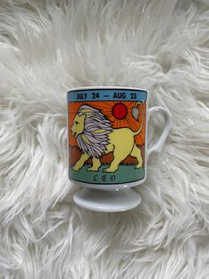 a coffee cup with a lion on it sitting on a fluffy white surface in the sun