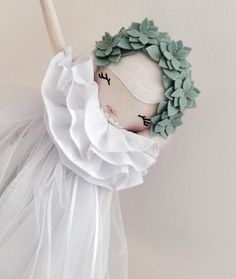 the doll is wearing a white dress and holding a wooden stick in her hand with green leaves on it