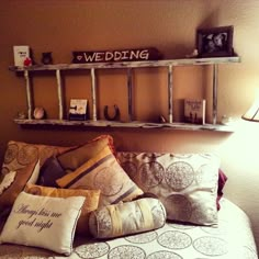 a bed topped with lots of pillows next to a wall mounted shelf filled with pictures