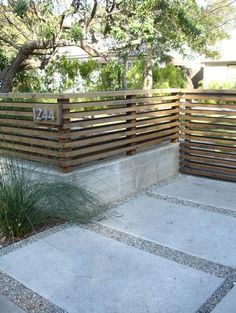 a wooden fence in the middle of a concrete area with grass and plants around it