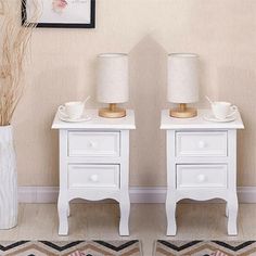 two white nightstands with lamps on top of them