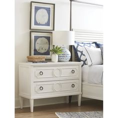 a white dresser sitting next to a bed with pictures on the wall above it and a lamp