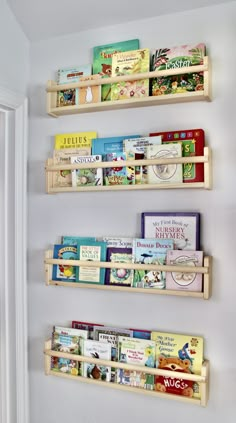 three wooden bookshelves with children's books on them against a white wall